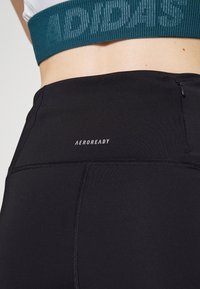 Leggings neri a vita alta con una texture liscia, dotati di un logo Aeroready e di una piccola tasca con zip sul retro.