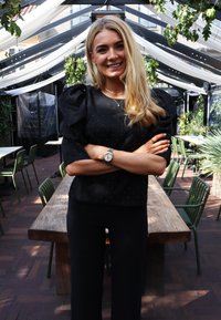 Čierny top s balónovými rukávmi a strieborným bodkovaným vzorom, skombinovaný s čiernymi nohavicami. V pozadí je textúrovaný drevený stôl a zelené stoličky.