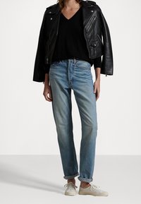 Svart lädermotorcykeljacka, svart topp med V-hals, ljusblå raka jeans och vita sneakers med strukturerade sulor.