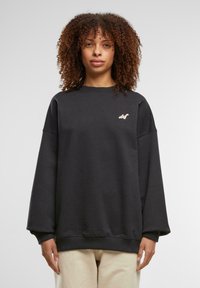 Mørk grå oversized sweatshirt med rund hals, senket skuldre og en liten brodert logo på brystet. Myk tekstur og ribbestrikkede mansjetter.