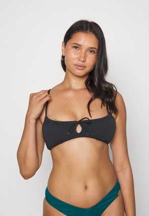 Top de biquíni preto texturizado com um buraco redondo e alças ajustáveis. Combinado com cuecas de biquíni azul-escuro.