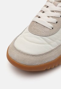 Sneaker med en lys grå semsket overdel med en glatt hvit nylonpanel, runde snøringer og en gummisåle.