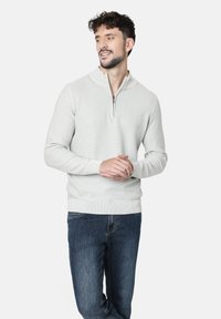 Suéter texturizado de color gris claro con cuello de media cremallera. Combinado con jeans de color azul oscuro. Presenta mangas largas y puños y dobladillo acanalados.