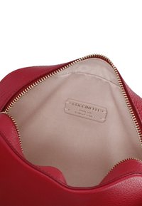 Interno di una borsa in pelle rossa con una texture liscia, zip dorata e un'etichetta che indica "Coccinelle Pelle Italiana Autentica."
