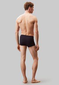 Czarne szorty kąpielowe o gładkiej teksturze i elastycznym pasie, dopasowany krój oraz minimalne zakrycie, pokazane z tyłu.