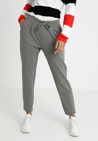 Lichtgrijze taps toelopende broek met een trekkoord in de taille, zijzakken en een gladde textuur, gecombineerd met een gestreepte trui en witte sneakers.