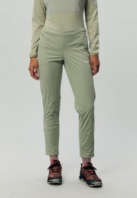 Pantaloni attivi slim-fit verdi chiari con vita elastica e tasche con zip. Indossati con scarpe scure con motivo strutturato.