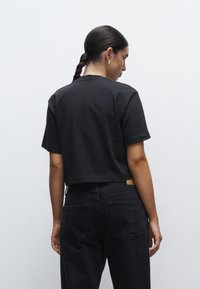 T-shirt nera cropped con maniche corte, realizzata in cotone. Abbinata a jeans neri a vita alta con tasche posteriori e una vestibilità larga.