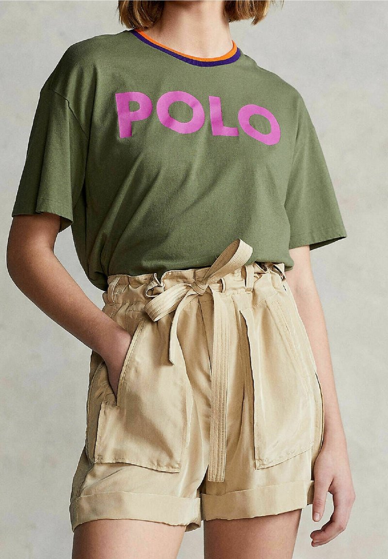 Olive green cotton t-shirt with large purple "POLO" print, paired with beige high-waisted shorts featuring a tied belt and side pockets.