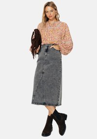 Blouse à motifs floraux rose et orange avec des manches volumineuses, associée à une jupe midi en denim grise et des bottines en daim marron.