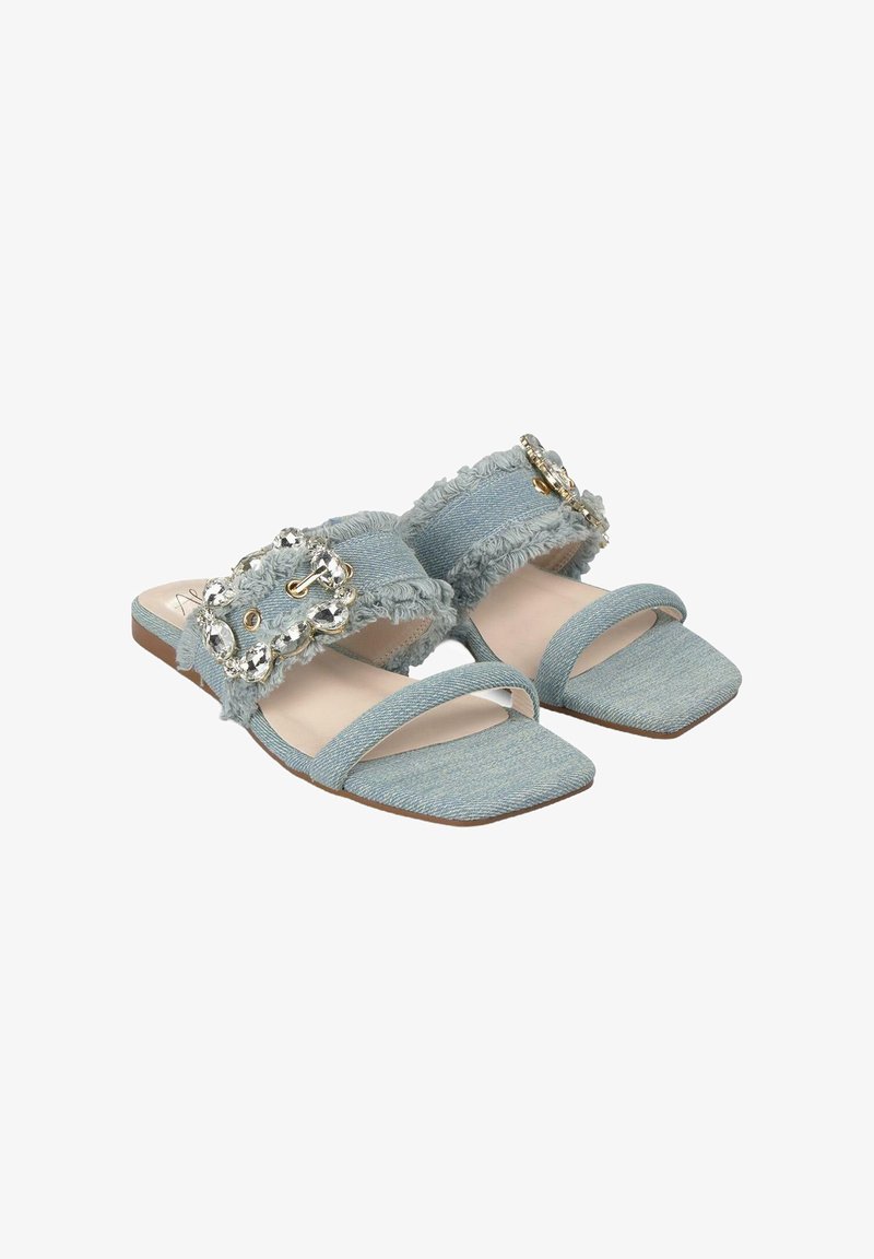 Sandali scivolati in denim blu con bordi sfilacciati, punta quadrata e una grande fibbia di gioielli come dettaglio distintivo. Tessuto morbido e suola piatta.