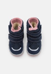 Baskets montantes bleu marine avec doublure rose, deux bandes Velcro ajustables, intérieur doux et semelle en caoutchouc texturé avec un accent blanc.