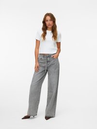 Grå denim bukser med vid ben og høy liv, parret med en tettsittende hvit t-skjorte i bomull. Modellen står med den ene hånden i lommen.