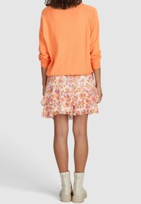 Orange stickad tröja med en avslappnad passform, kombinerad med en flerlagersblommig kjol i mjuka pastellfärger. Omfångsrika vita ankelstövlar.