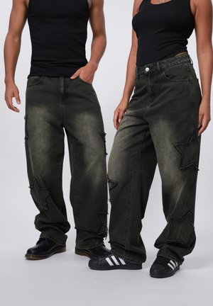 Baggy, dark green jeans with star-shaped cutouts and frayed edges. Worn with black shoes; textured fabric visible. Plain background.