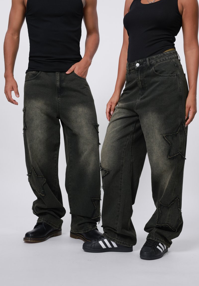 Baggy, dark green jeans with star-shaped cutouts and frayed edges. Worn with black shoes; textured fabric visible. Plain background.