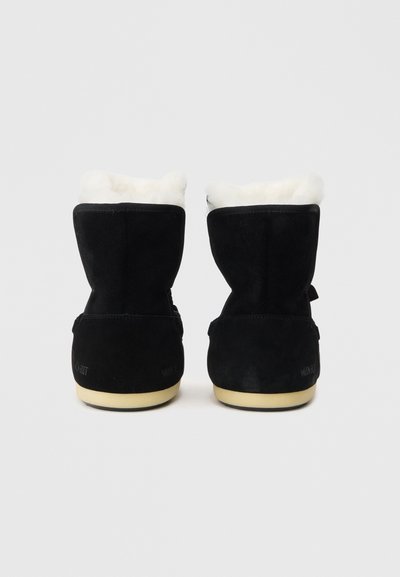 Bottines noires en daim, dotées d'une doublure en fausse fourrure blanche, d'une forme arrondie et d'une semelle en caoutchouc beige avec un branding minimal à l'arrière.