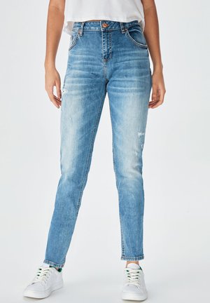 Jean en denim léger taille haute, de couleur bleu clair, avec une coupe slim, comportant des zones usées et un design classique à cinq poches. Baskets blanches incluses.