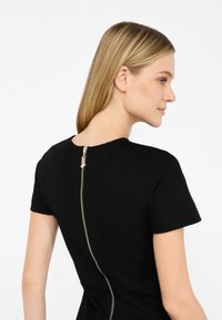 Abito nero con maniche corte e zip sul retro con dettagli in oro. Il tessuto sembra liscio e aderente.