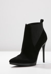 Stivale ankle nero in suede con punta a punta, tacco stiletto alto e pannelli elastici sui lati per una facile vestibilità.