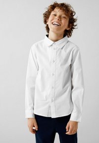 Camicia bianca con bottoni, maniche lunghe e colletto a punta, realizzata in morbido tessuto di cotone. Presenta un logo discreto sul petto e un design pulito.