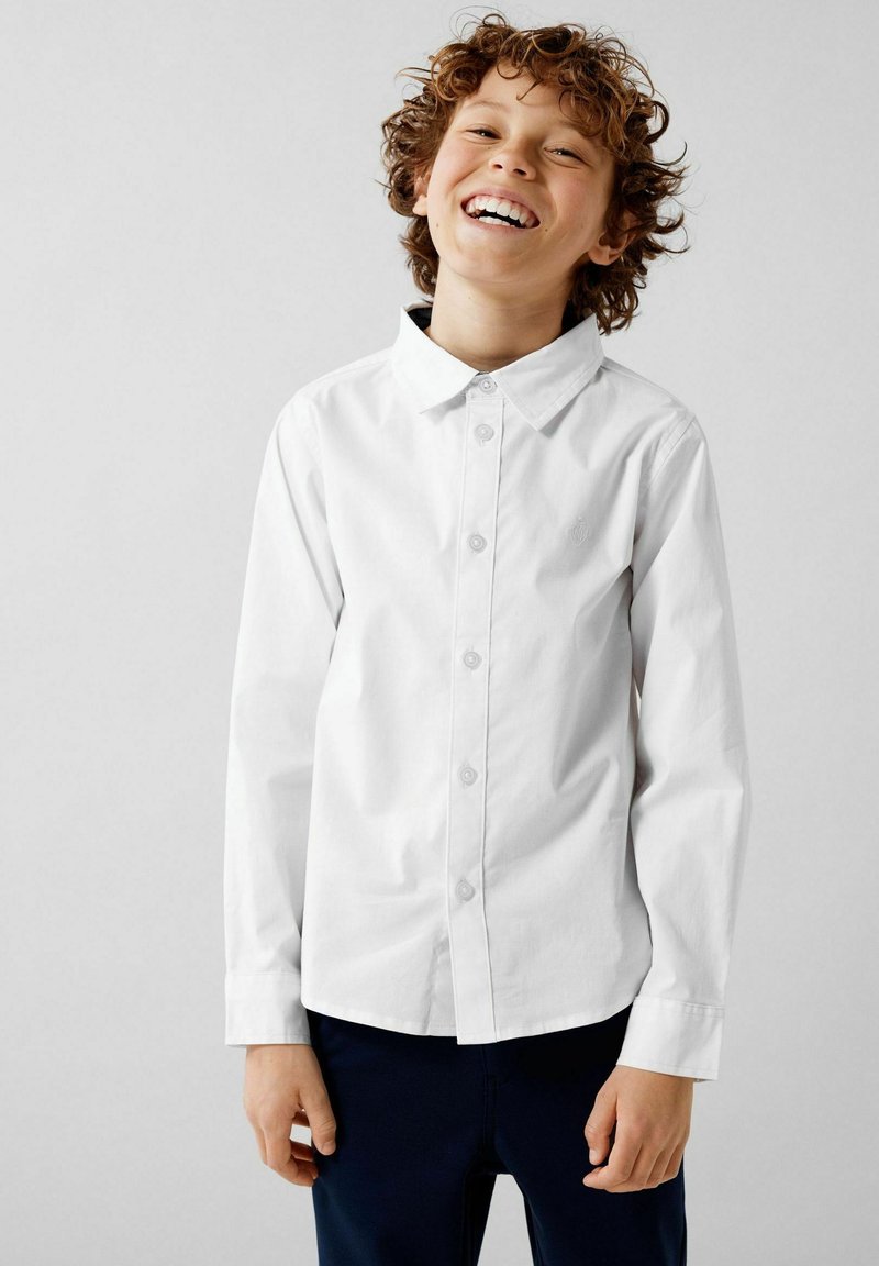 Camicia bianca con bottoni, maniche lunghe e colletto a punta, realizzata in morbido tessuto di cotone. Presenta un logo discreto sul petto e un design pulito.