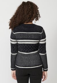 Stickad tröja med marinblå och grå färgskala, tydliga vita ränder och diamantmönster. Långa ärmar, rund halsringning, texturerat tyg.