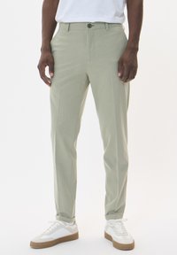 Light green tailored trousers with a smooth texture, featuring a front button closure and straight legs, paired with white sneakers.