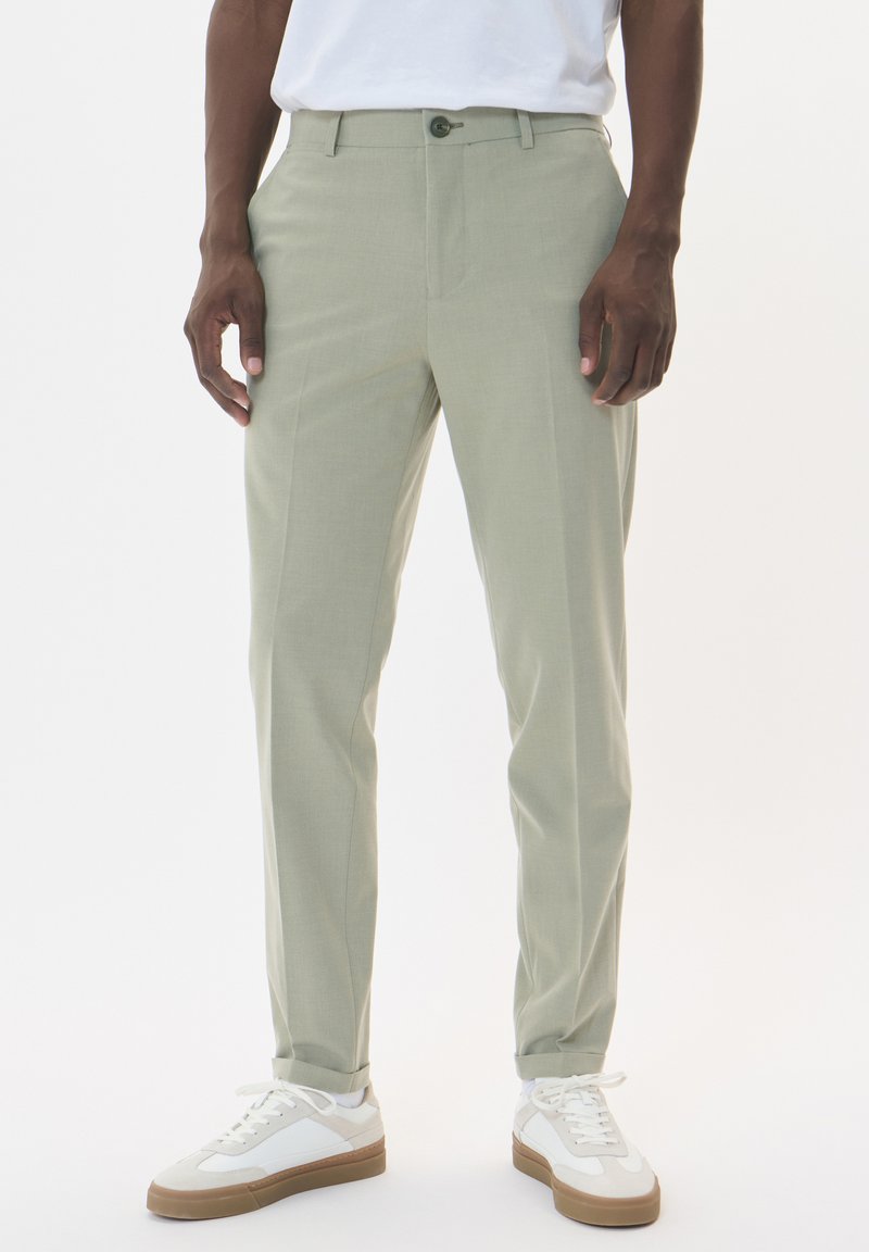 Light green tailored trousers with a smooth texture, featuring a front button closure and straight legs, paired with white sneakers.