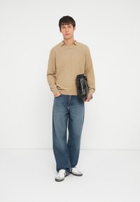 Beżowy sweter polo z teksturowanym splotem, luźne niebieskie dżinsy, czarna torba z metalowymi akcentami oraz białe sneakersy z szarymi detalami.