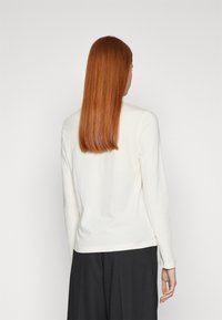 Langärmliges Creme-Top aus weichem Stoff, mit geradem Schnitt, Rundhals und einem etwas längeren Rückensaum. Keine sichtbaren Muster.