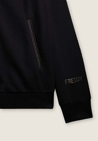 Felpa nera con una texture liscia, dotata di tasca con zip e con "FREDDY" ricamato in accenti metallici sulla manica.