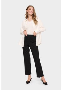 Bela srajca z gumbi čez preprosto majico, kombinirana s črnimi širokimi hlačami in črnimi koničastimi petami. Tkanina je videti gladka in lahka.