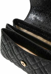 Sac à main matelassé noir avec motif monogramme, trois compartiments et fermeture à pression dorée. Doublure intérieure lisse.