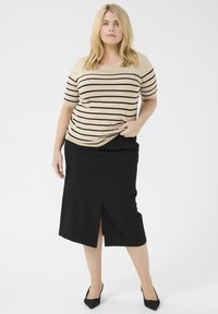 Top in maglia a righe beige e nere con maniche corte abbinato a una gonna nera al ginocchio con uno spacco frontale. Tacchi neri a punta.