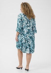 Robe à manches courtes en teal et imprimé animal blanc, avec un ourlet à volants en couches et une coupe décontractée. Portée avec des chaussures noires à enfiler.