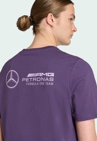 Paarse katoenen T-shirt, met een wit logo met "AMG PETRONAS FORMULA ONE TEAM" op de achterkant. Klassieke pasvorm, korte mouwen, zachte textuur.