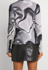 Langarmshirt in Grau und Schwarz mit einem wellenförmigen abstrakten Design. Kombiniert mit einem schwarzen Minirock aus Kunstleder. Glatte Textur insgesamt.