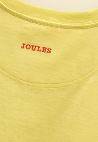 Encolure en tissu jaune avec le nom de la marque brodé en rouge "JOULES" centré sous la couture du col.