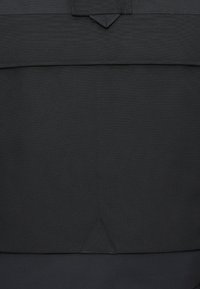 Saco de tecido preto, texturizado, com fecho de aba. Apresenta um destaque triangular na parte inferior. Design simples, sem logótipos ou padrões visíveis.