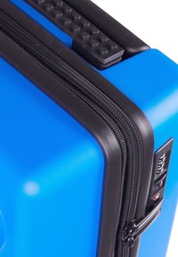 Blue hard-shell suitcase with black zippers, textured handle, and combination lock. Smooth finish with a rectangular shape.