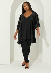 Musta kimono-tyylinen takki lyhyillä hihoilla, koristeltu hopeisilla tähdillä. Päällä musta toppi ja housut, viimeistelty mustilla sandaaleilla.