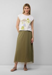 Weißes kurzärmeliges Hemd mit einem bunten Strandmotiv, kombiniert mit einem langen olivgrünen Faltenrock und beigen flachen Sandalen mit Riemen.