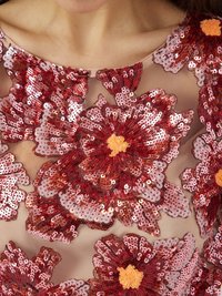 Des appliqués de fleurs en sequins rouges sur un tissu transparent créent un design texturé et superposé. Les fleurs présentent des centres de nuances variées de rouge et d'orange.