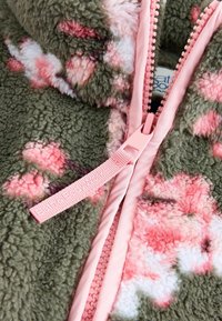 Fleece bunda v olivově zelené barvě s růžovým květinovým vzorem, vybavená růžovým zipem a štítkem značky. Měkká, strukturovaná tkanina.