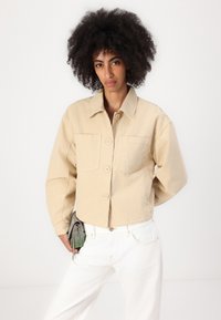 Casaco cropped bege com gola, quatro botões e dois bolsos frontais, feito de tecido texturizado com needled.