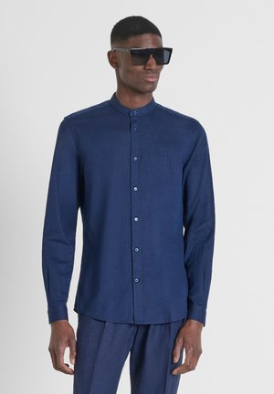 Camicia navy con bottoni, colletto, e maniche lunghe, con un ricamo del logo discreto. Realizzata in tessuto leggero, presenta una texture liscia.