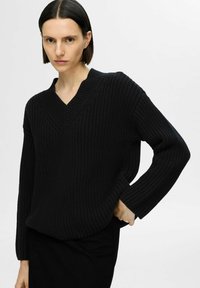 Maglione nero lavorato a maglia con scollo a V, texture a coste e maniche lunghe, abbinato a una gonna nera aderente.