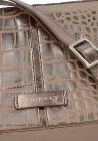 Borsa in bronzo metallizzato con texture a coccodrillo, base liscia e un accento in argento con etichetta a marchio "BURKELY."