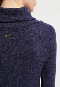 Marineblå, texturerad tröja med vikkrage. Har en liten "smash!" logotag på baksidan. Sömmarna är synliga på axlarna.